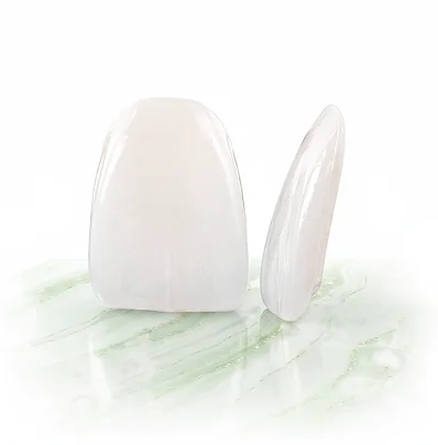Two white ultra-thin dental veneers resting on a light green marble surface, one showing its front and the other its thin side profile.
